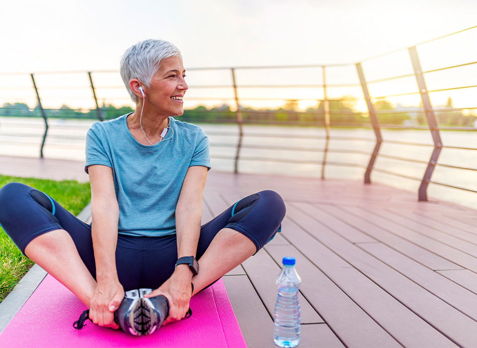 a woman sitting outdoors on a yoga mat