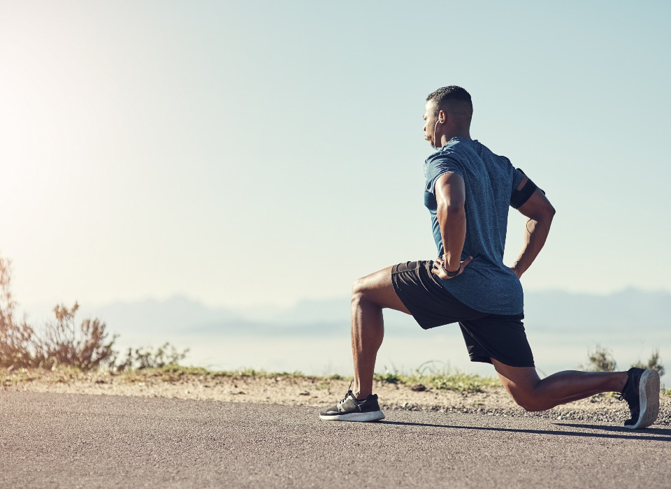 a man does a lunge along the edge of a road, looking like he's warming up before running