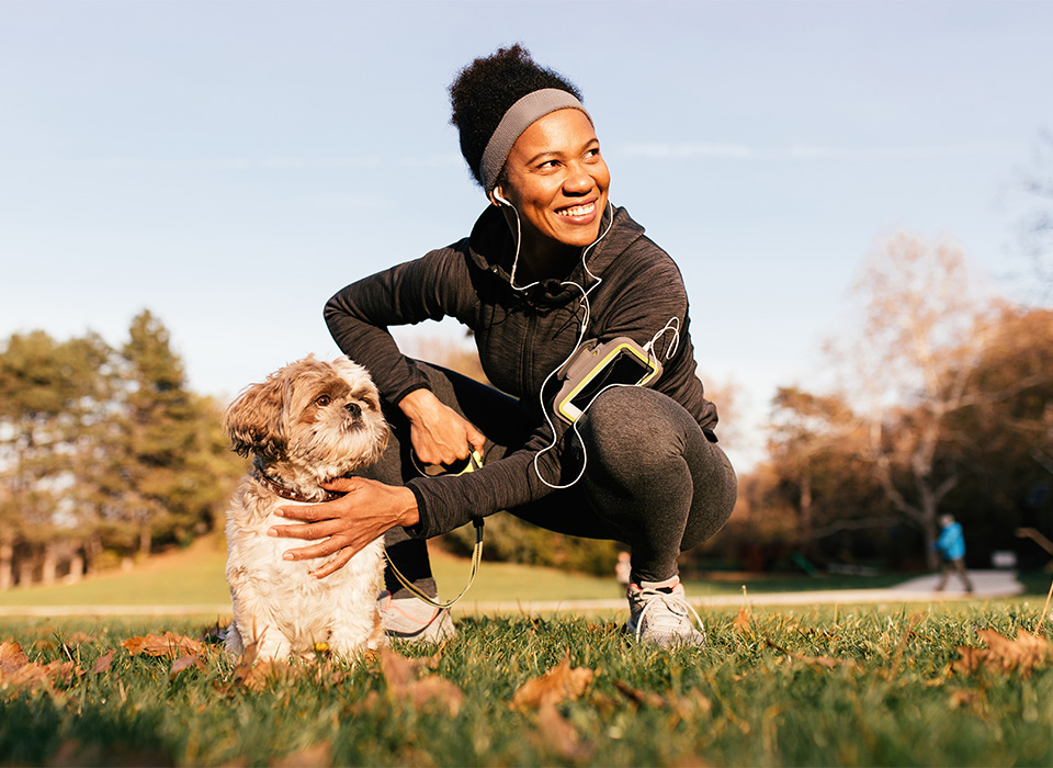 woman in exercise clothes crouching down and petting a dog