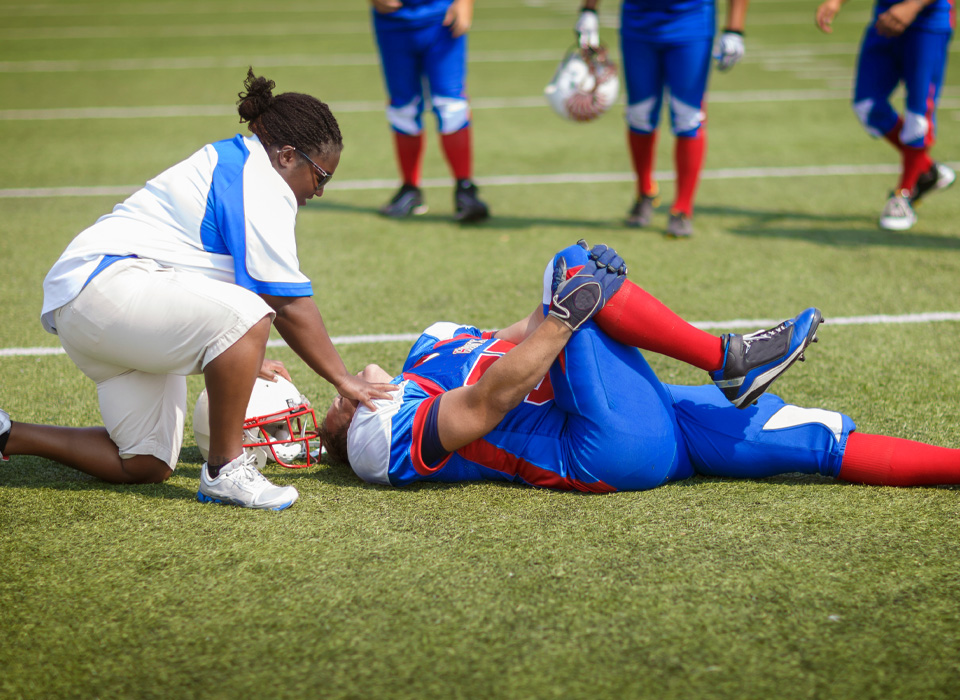 an injured football player on the field, with a medical provider checking with him