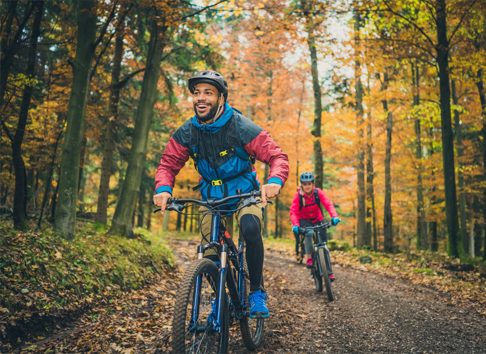 two people in rain gear bike on a wooded bike path in fall
