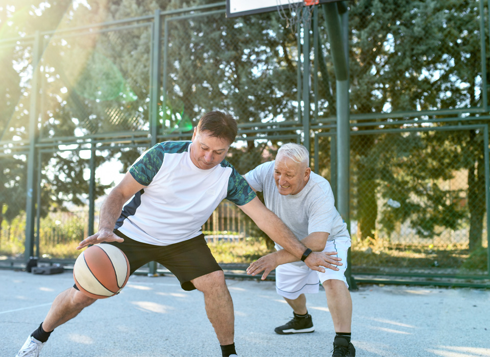 two older men play basketball on an outdoor court