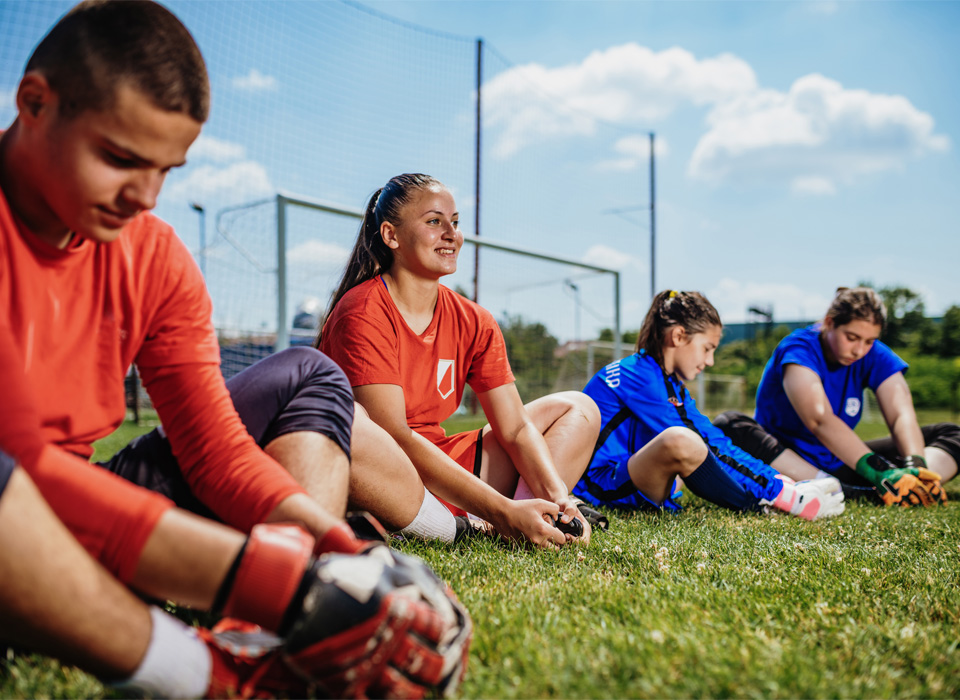 a group of teenagers in sports uniforms stretch their legs