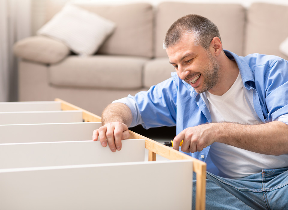 a man sits on the living room floor and puts together flat pack furniture