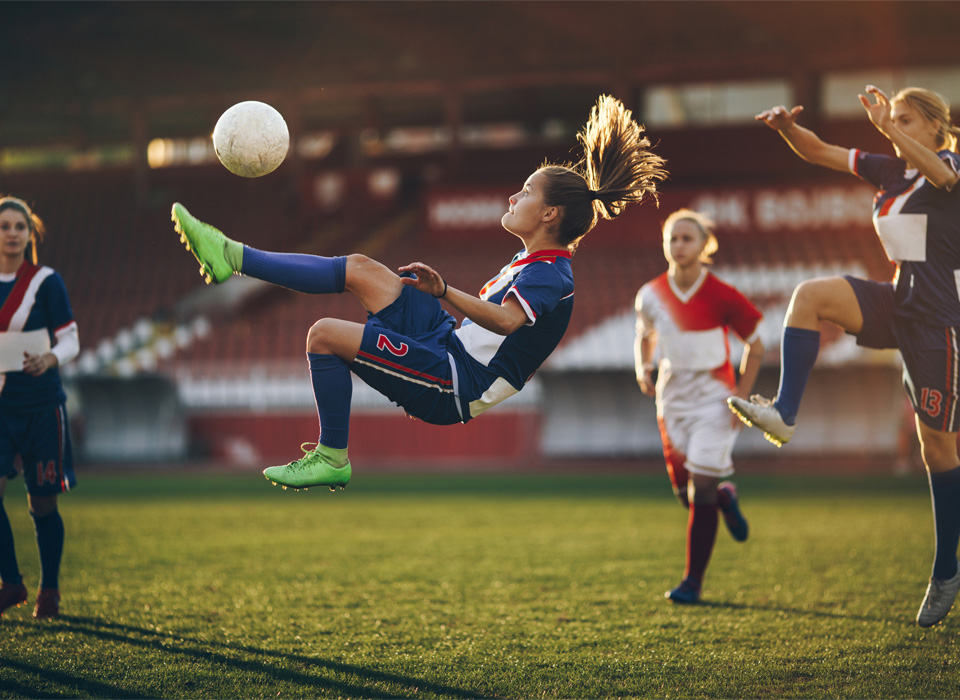 a soccer player is in the air as she tries to kick a ball during a game