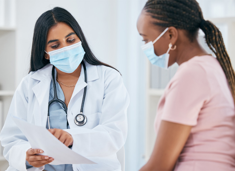 A medical provider points out something to her patient. Both are wearing surgical masks.