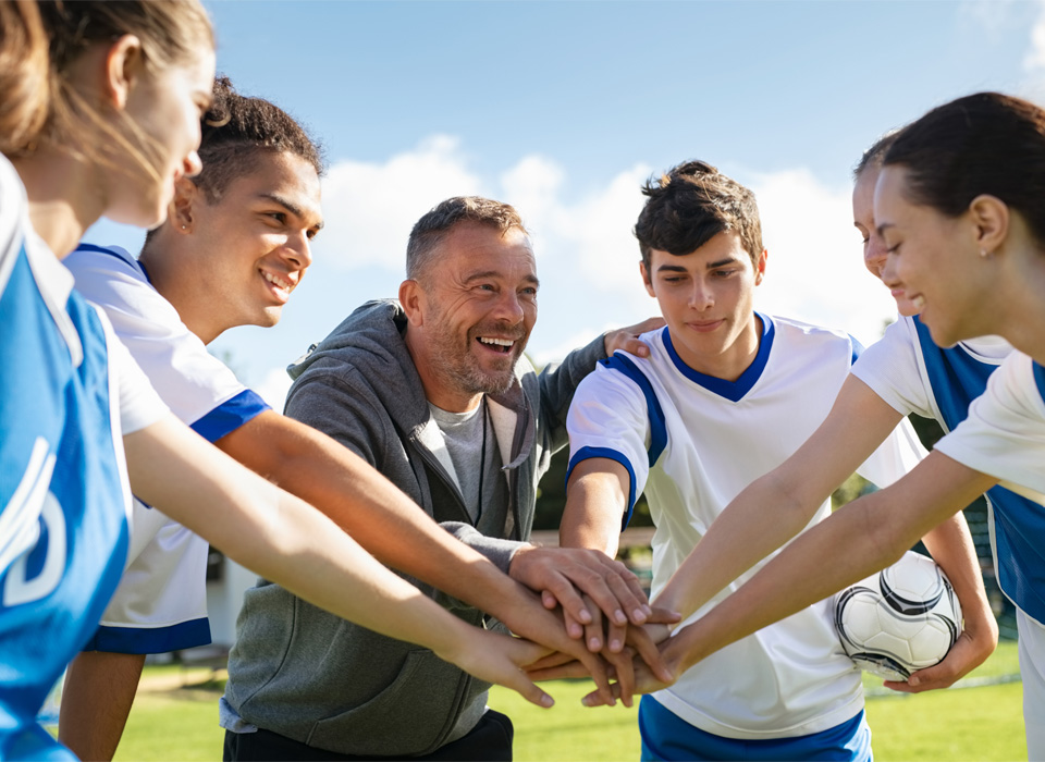 a coach and teenage soccer players put their hands in for good luck