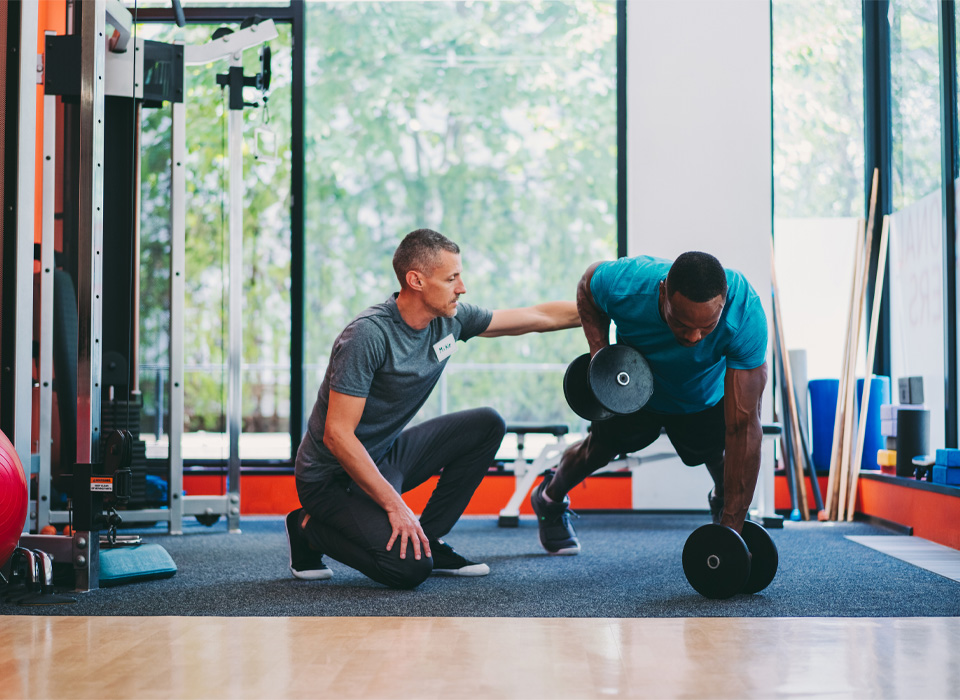 a personal trainer guides a man doing a dumbbell workout