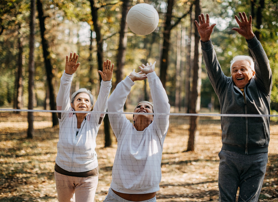 three older adults are trying to hit a volleyball outside