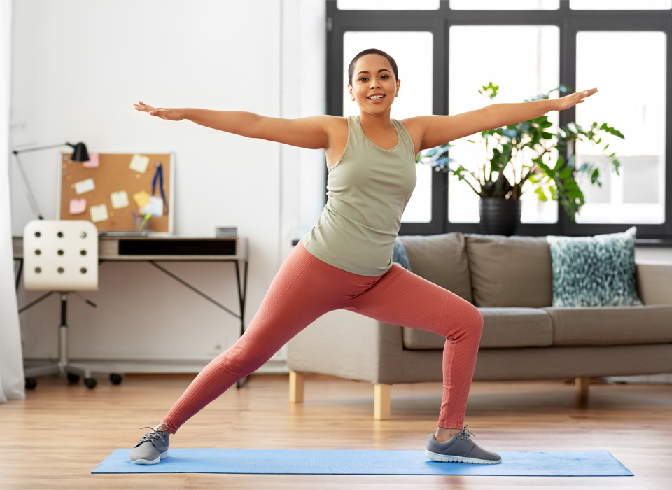 a woman standing, holding a yoga pose on a yoga mat in her living room