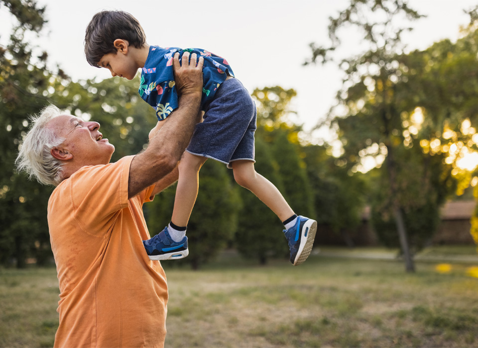 older man holds a three year old boy up in the air