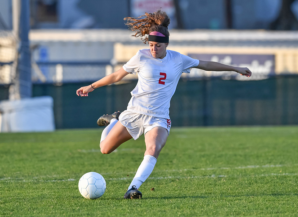 woman in white soccer uniform about to kick a soccer ball