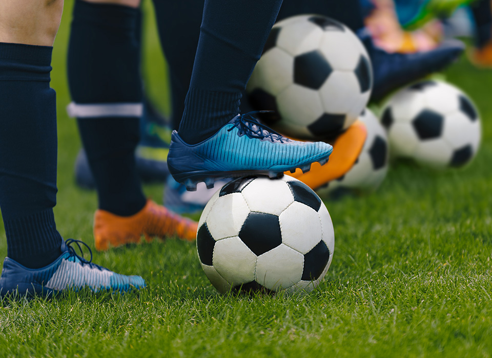 feet in soccer cleats with one foot on a black and white soccer ball