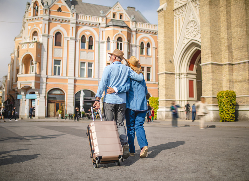 man and woman with their arms around each other, man rolling a suitcase, in a European city center