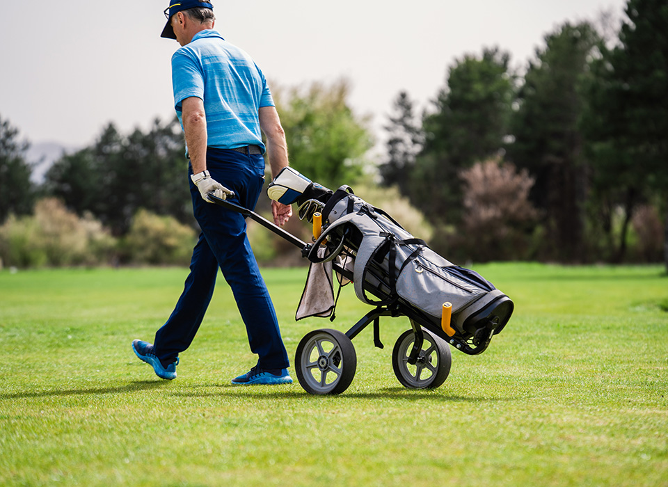 golfer rolling his clubs on a rolling cart behind him, on a golf course
